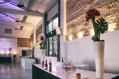 Salle de réception décorée pour un mariage, avec tables rondes, nappes blanches et guirlandes lumineuses au plafond.