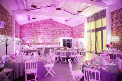 Salle de réception décorée pour un mariage, avec tables rondes, nappes blanches et guirlandes lumineuses au plafond.
