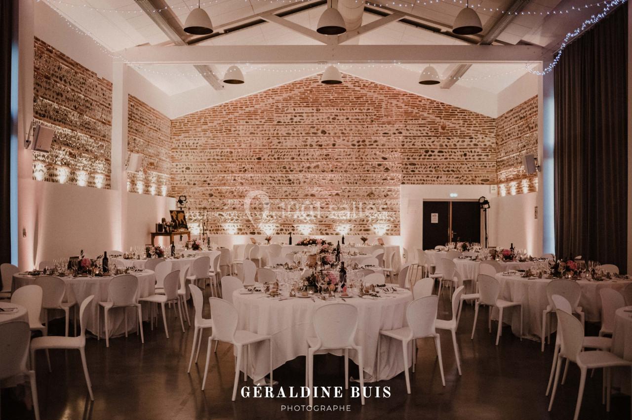 Salle de réception décorée avec des tables rondes, nappes blanches, chaises modernes et éclairage tamisé.