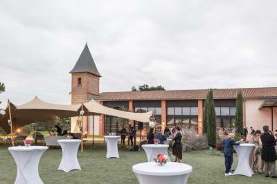 Salle de réception décorée pour un mariage, avec tables rondes, nappes blanches et guirlandes lumineuses au plafond.