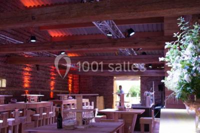 Salle de réception décorée pour un mariage, avec tables rondes, nappes blanches et guirlandes lumineuses au plafond.