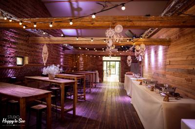 Salle de réception décorée pour un mariage, avec tables rondes, nappes blanches et guirlandes lumineuses au plafond.