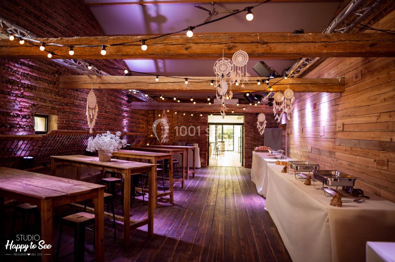 Salle en bois avec tables hautes, guirlandes lumineuses, attrape-rêves suspendus et buffet dressé sur le côté.