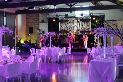 Salle de réception décorée pour un mariage, avec tables rondes, nappes blanches et guirlandes lumineuses au plafond.