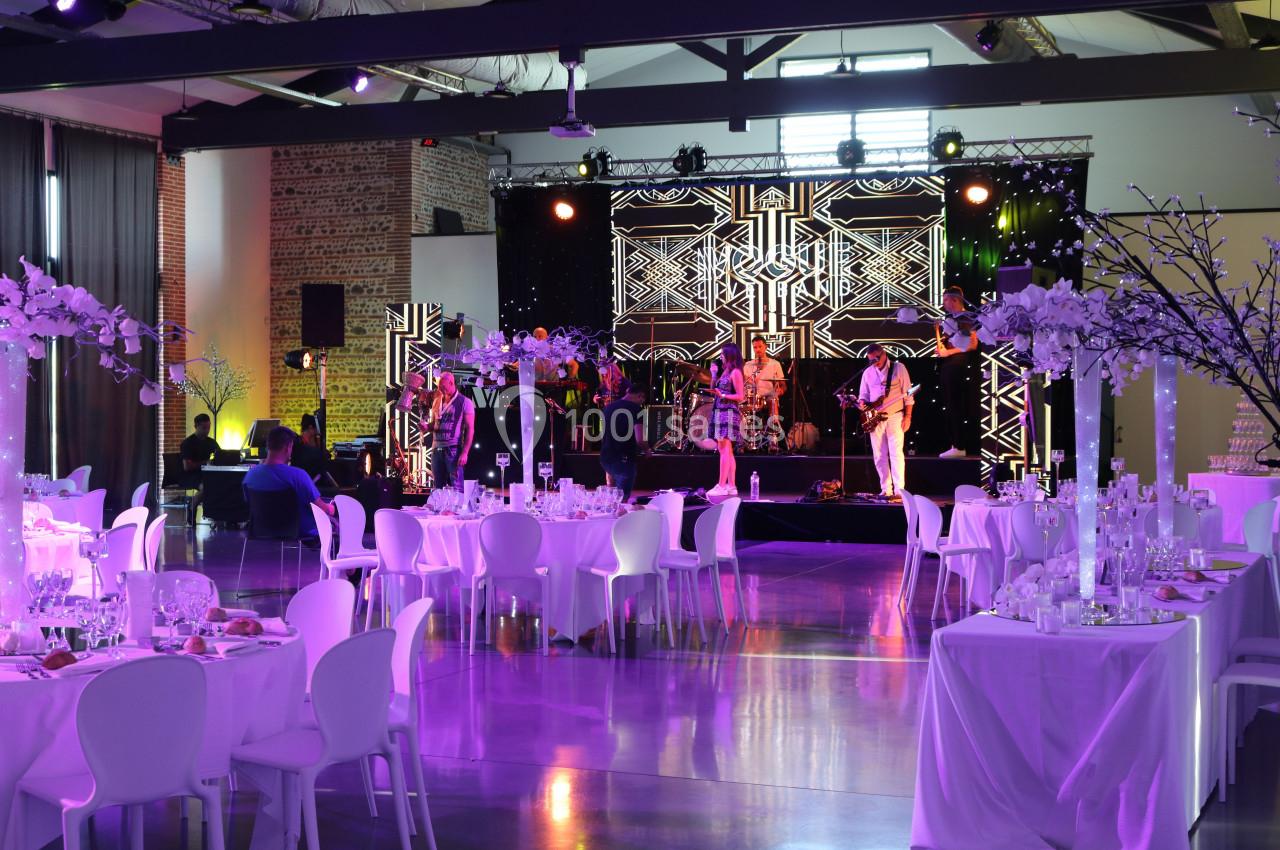 Salle de réception décorée avec des tables élégantes et un groupe de musique jouant sur une scène illuminée.