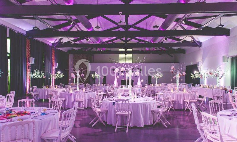 Salle de réception décorée avec des tables rondes, chaises blanches et éclairage violet.