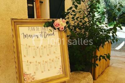 Un couple habillé élégamment, la femme en robe blanche et l'homme en costume, pose dans une pièce lumineuse.