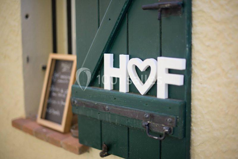 Volet vert entrouvert avec des lettres blanches formant ’H♥F’ posées dessus, tableau noir en arrière-plan.