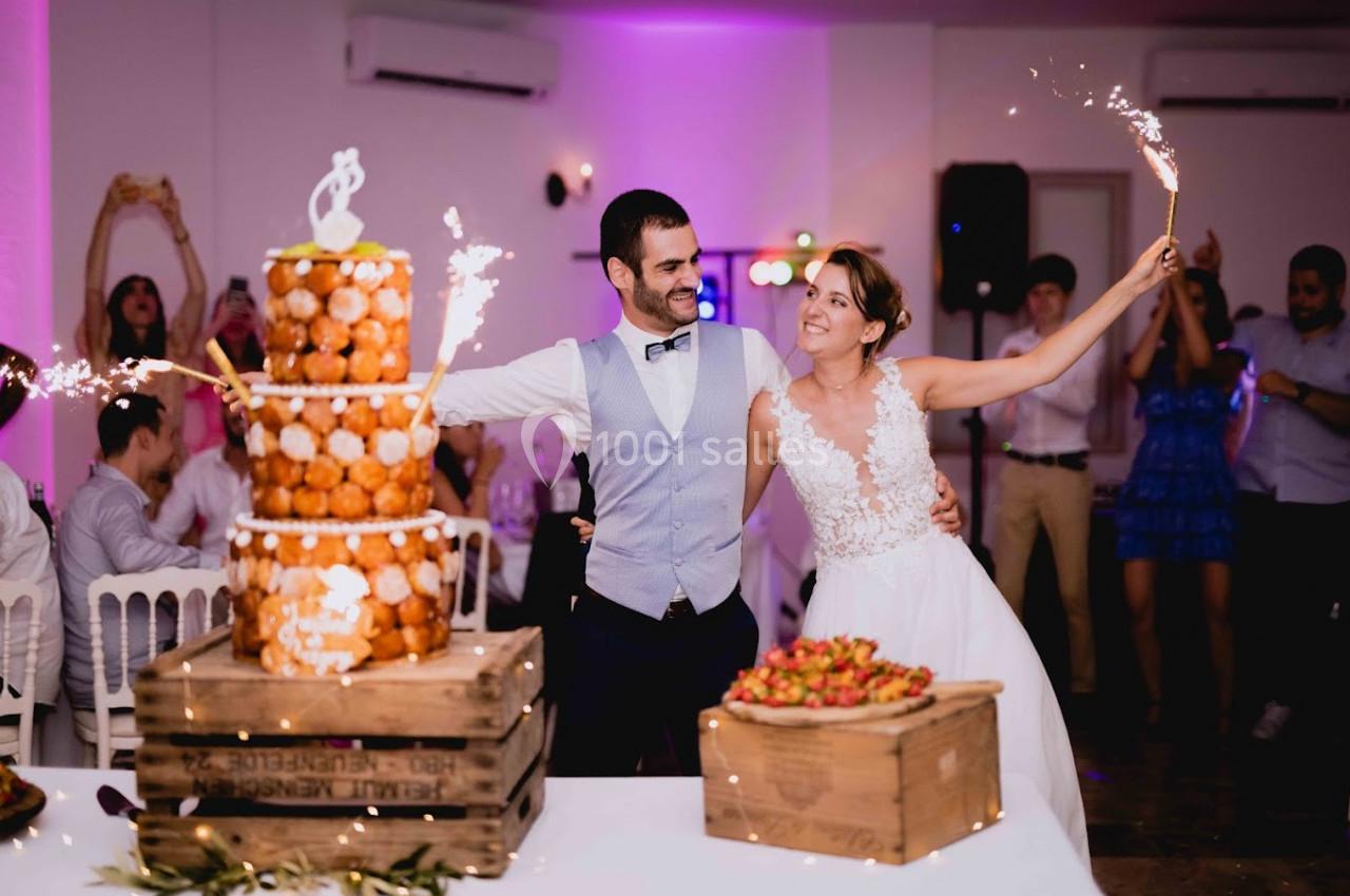 Un couple de mariés souriants tient des cierges magiques près d'une pièce montée et de fraises lors de leur réception.