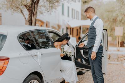 Un couple habillé élégamment, la femme en robe blanche et l'homme en costume, pose dans une pièce lumineuse.