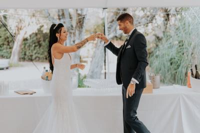 Un couple habillé élégamment, la femme en robe blanche et l'homme en costume, pose dans une pièce lumineuse.