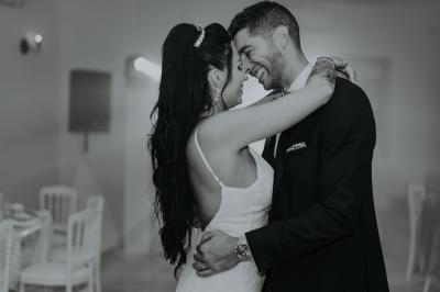 Un couple habillé élégamment, la femme en robe blanche et l'homme en costume, pose dans une pièce lumineuse.