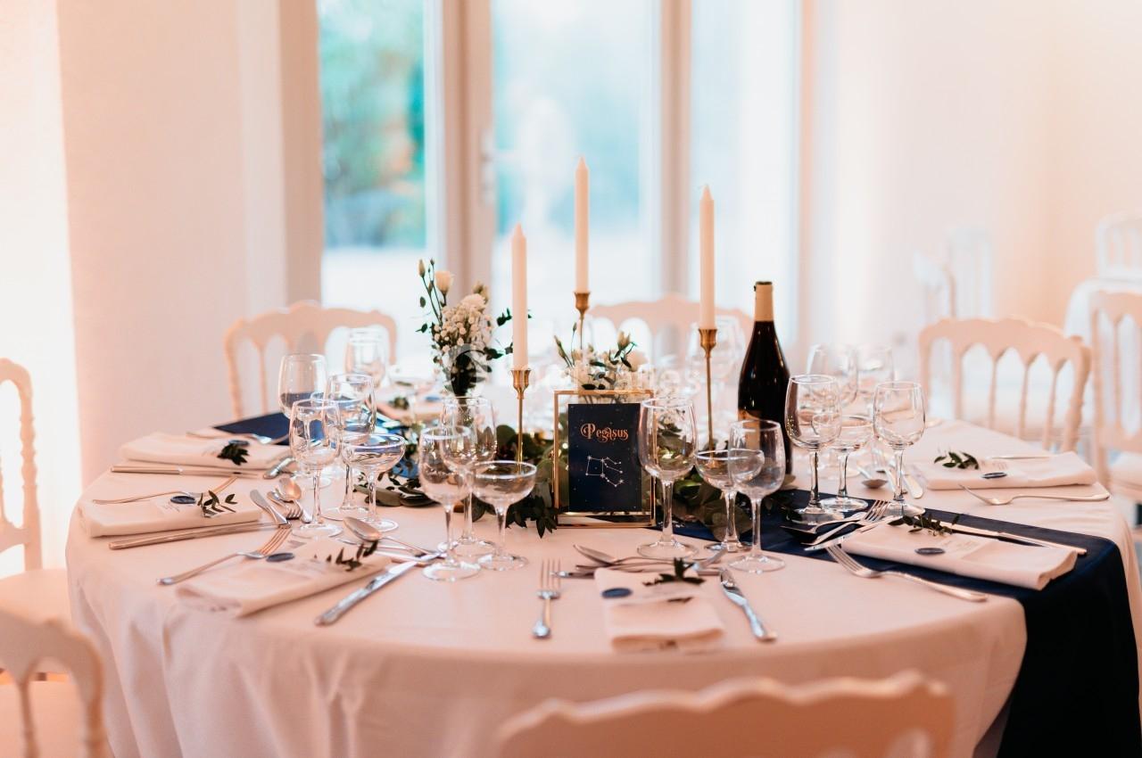 Table élégamment dressée avec nappes blanches, bougies, vaisselle raffinée et décoration florale.