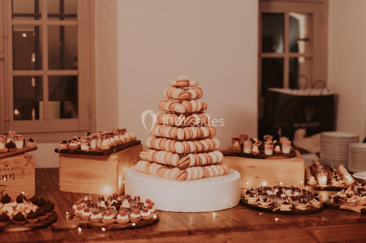 Tour de macarons sur une table en bois entourée de petits desserts variés dans une salle éclairée chaleureusement.