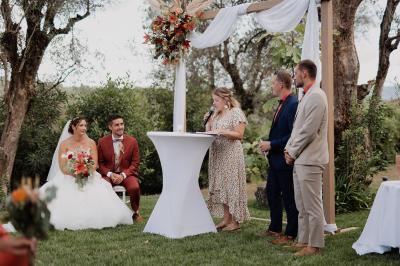 Un couple habillé élégamment, la femme en robe blanche et l'homme en costume, pose dans une pièce lumineuse.
