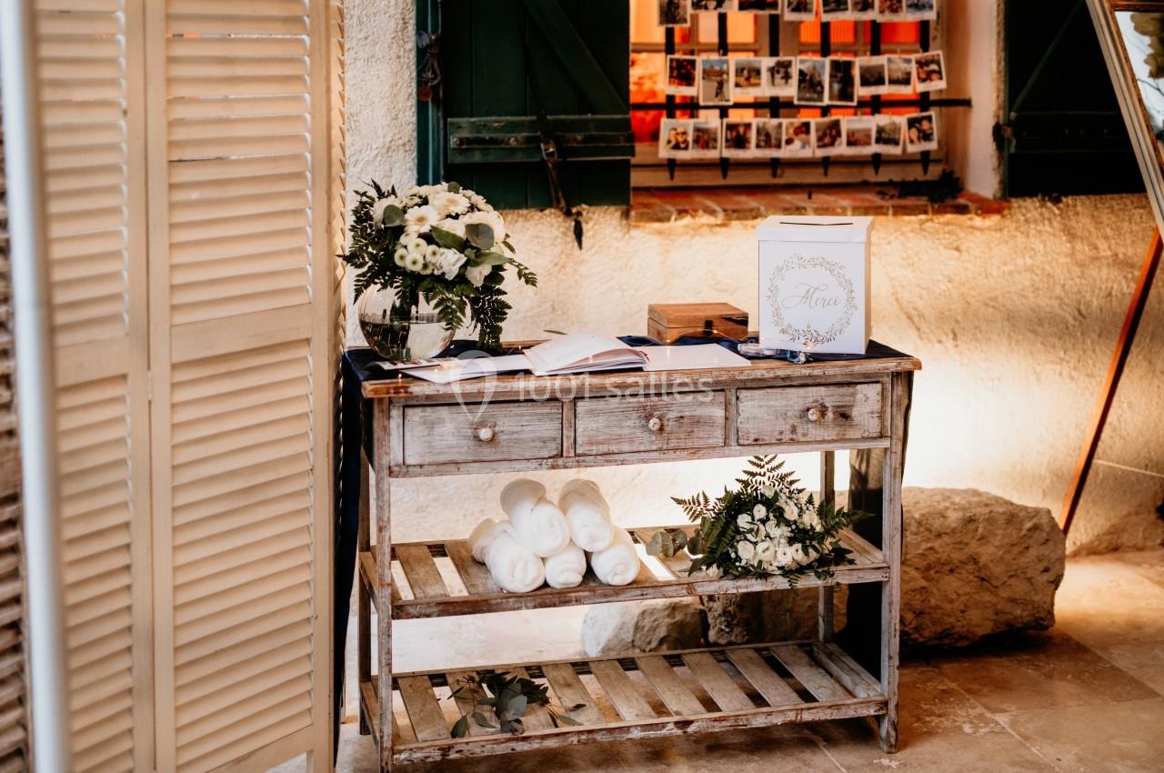 Table en bois décorée avec des fleurs blanches, des serviettes roulées et une urne, dans un cadre rustique.