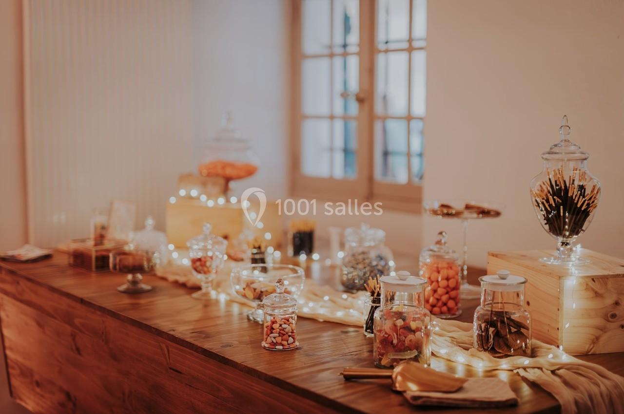 Table en bois décorée avec des bocaux de bonbons variés, guirlandes lumineuses et accessoires de fête.