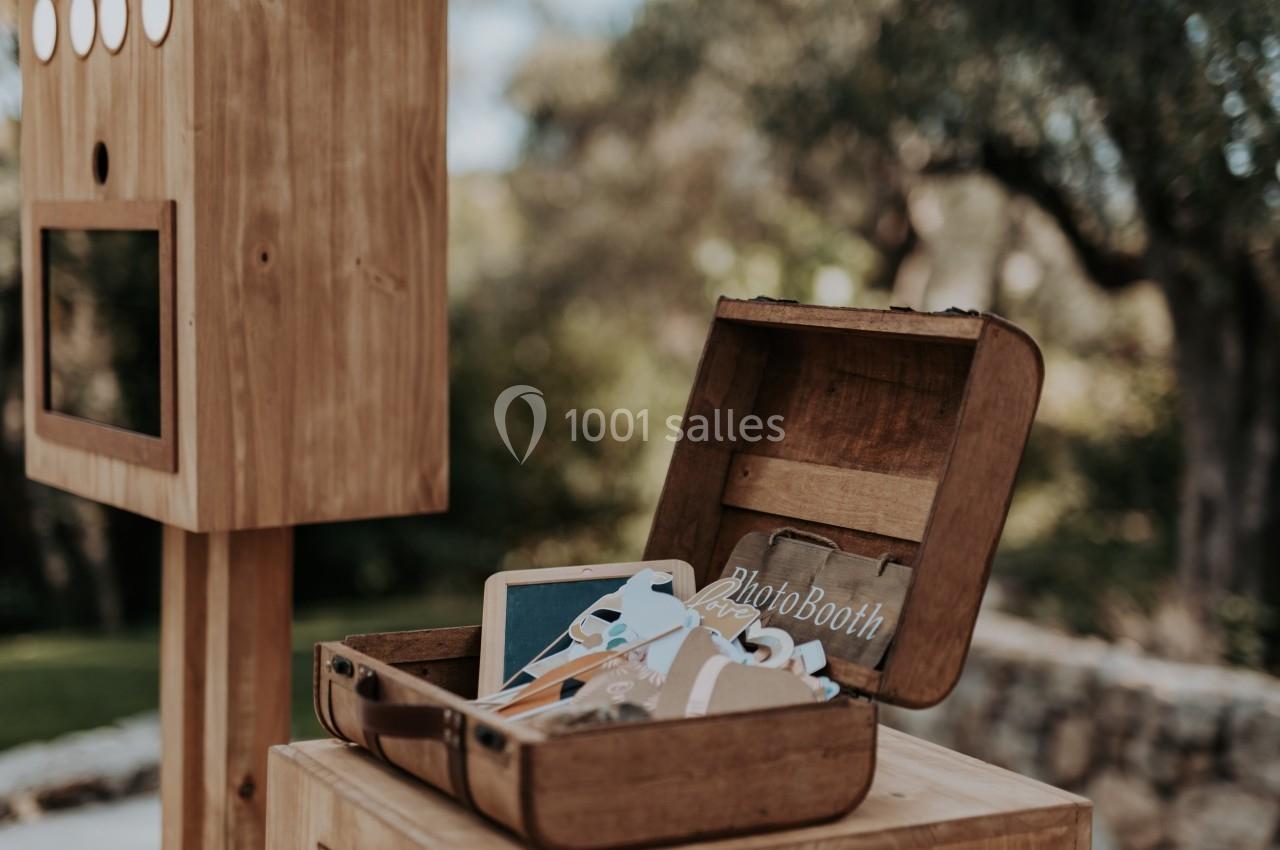Boîte en bois ouverte contenant des accessoires de photobooth, posée sur une table en extérieur près d'une cabine photo.