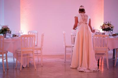 Un couple habillé élégamment, la femme en robe blanche et l'homme en costume, pose dans une pièce lumineuse.
