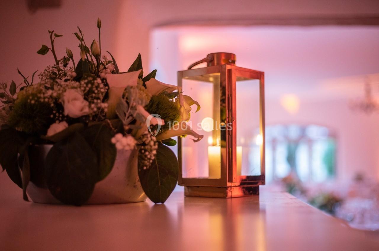 Bouquet de fleurs blanches et vertes à côté d'une lanterne dorée contenant une bougie allumée, dans une ambiance tamisée.