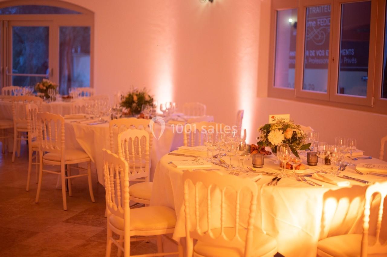 Salle de réception élégante avec tables rondes dressées, nappes blanches et décoration florale.