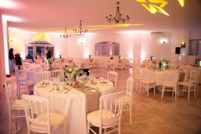 Un couple habillé élégamment, la femme en robe blanche et l'homme en costume, pose dans une pièce lumineuse.