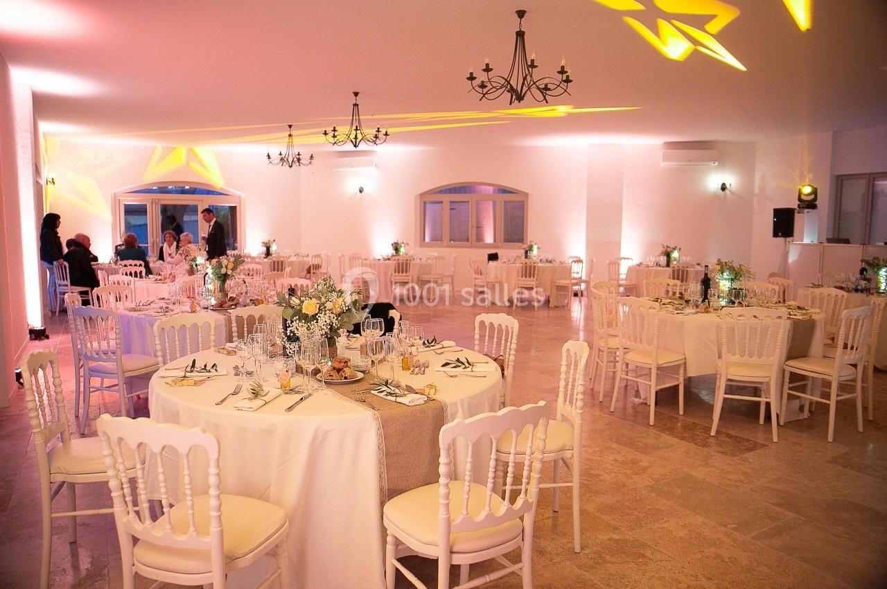 Salle de réception élégamment décorée avec des tables rondes, nappes blanches, chaises assorties et éclairage chaleureux.