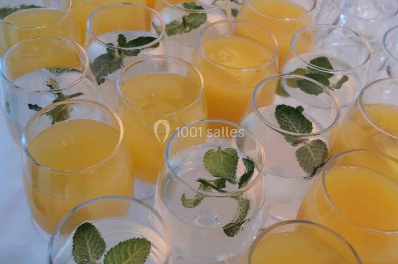 Verres de jus d'orange et d'eau garnie de feuilles de menthe disposés sur une table blanche.
