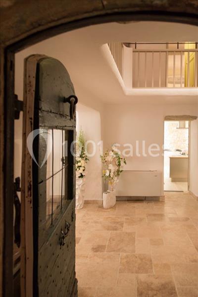 Vue intérieure d'une pièce lumineuse avec sol en pierre, porte ancienne ouverte et décorations florales blanches.