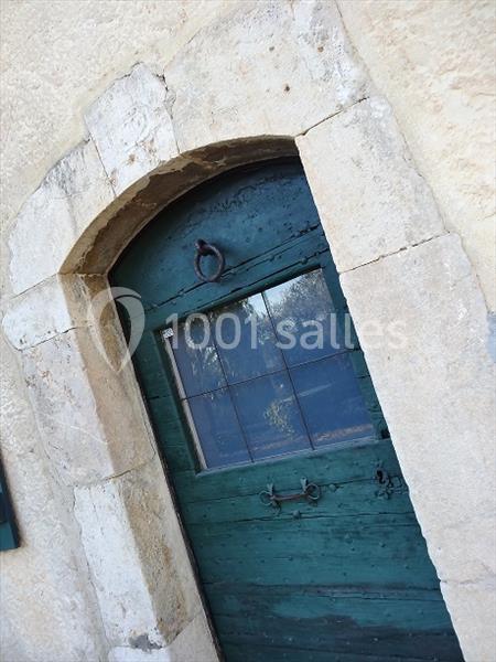 Porte en bois bleue vieillie avec une petite fenêtre vitrée et un encadrement en pierre claire.