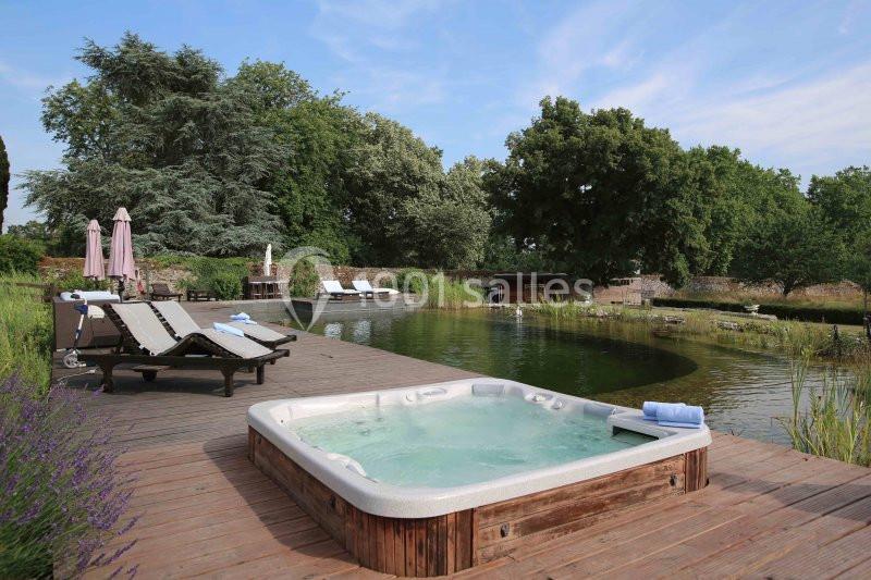 Bain à remous sur une terrasse en bois près d'un étang naturel, entouré de chaises longues et de végétation.