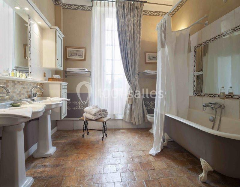 Salle de bain lumineuse avec baignoire sur pieds, double vasque, carrelage en terre cuite et rideaux élégants.