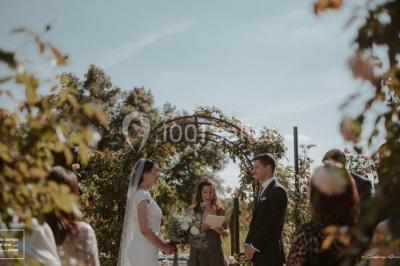 Bouquet de fleurs blanches et roses dans un pichet en terre cuite, posé dans une caisse en bois entourée de verdure.