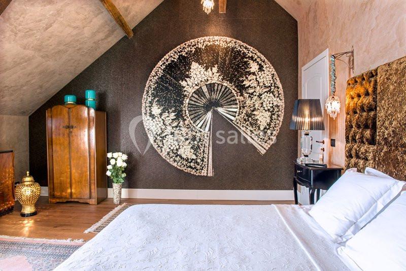 Chambre décorée avec un grand motif mural circulaire, mobilier en bois, lit avec tête de lit capitonnée et éclairage…