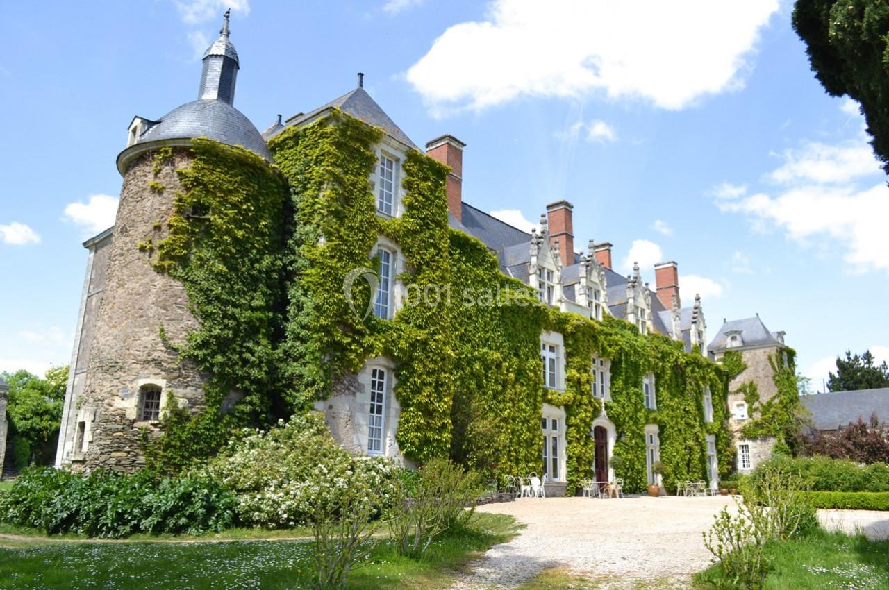Façade d'un château en pierre recouvert de lierre, avec une tour ronde et un ciel bleu en arrière-plan.