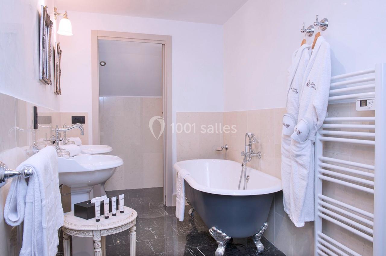 Salle de bain avec baignoire sur pieds, double vasque, radiateur sèche-serviettes et peignoirs accrochés.