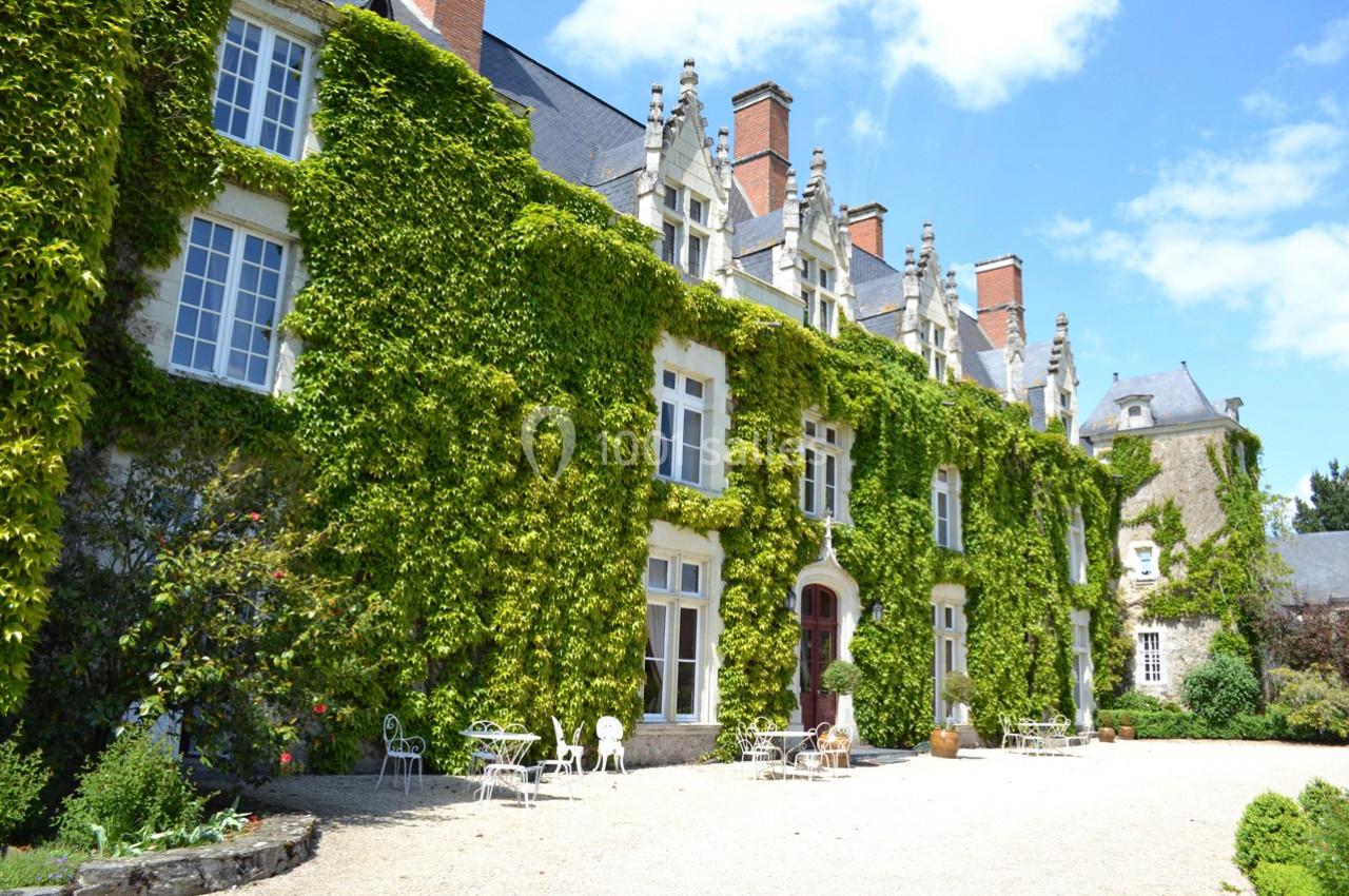 Façade d'un manoir couvert de lierre avec des fenêtres à croisillons, entouré d'un jardin et de mobilier d'extérieur.