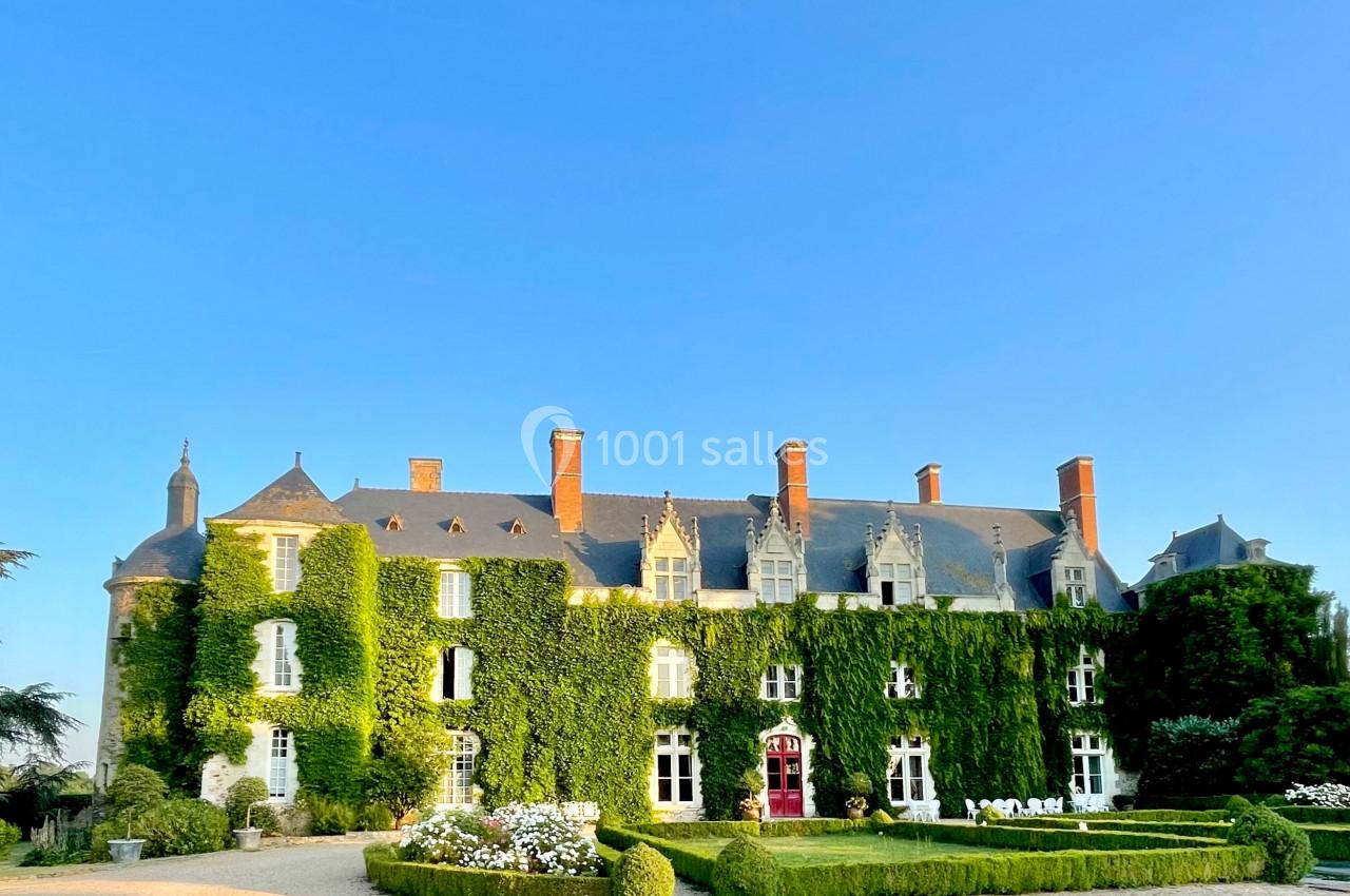 Façade d'un château recouvert de lierre, entouré de jardins fleuris et baigné par une lumière ensoleillée.