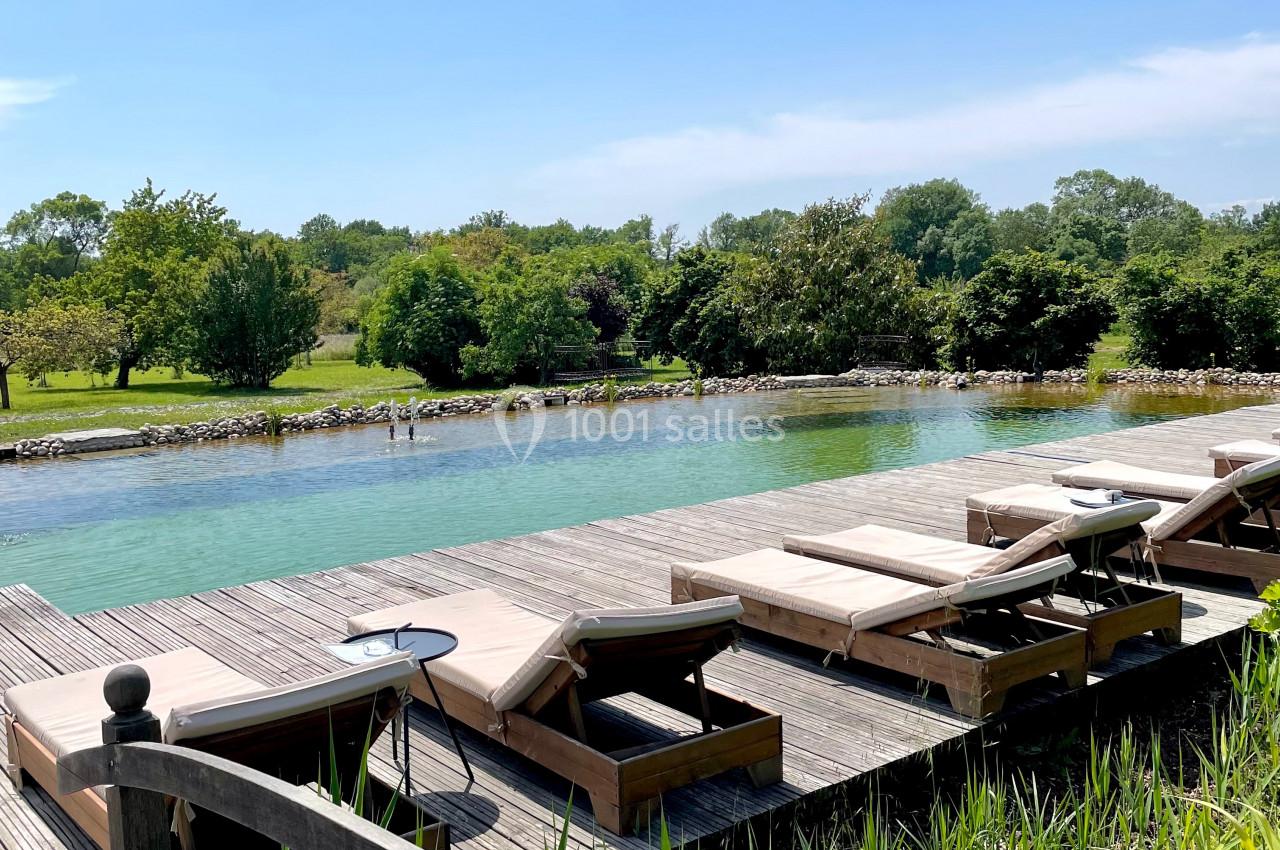 Chaises longues en bois alignées sur une terrasse près d'une piscine naturelle entourée de verdure.