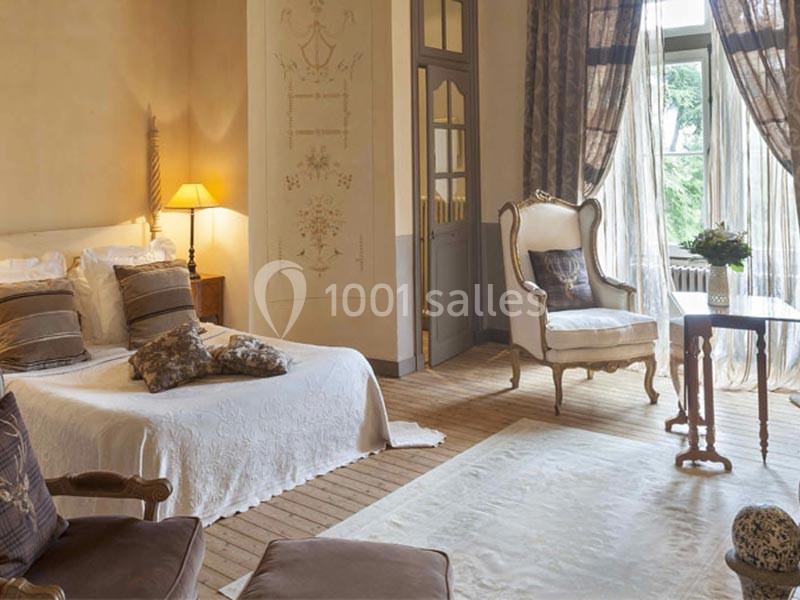 Chambre lumineuse avec lit double, fauteuil, table basse et grandes fenêtres donnant sur un jardin verdoyant.