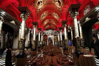 Salle élégante avec tables rondes dressées, chaises blanches et grand portrait en noir et blanc en arrière-plan.