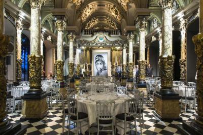 Salle élégante avec tables rondes dressées, chaises blanches et grand portrait en noir et blanc en arrière-plan.