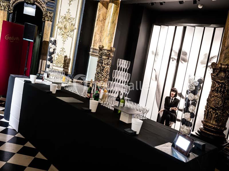 Table dressée avec des verres et des bouteilles dans un décor élégant, avec une personne assise en arrière-plan.