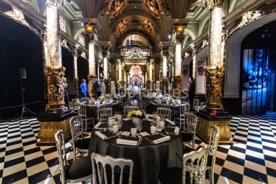 Salle élégante avec tables rondes dressées, chaises blanches et grand portrait en noir et blanc en arrière-plan.