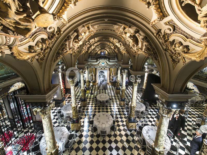 Salle ornée de colonnes et de voûtes décorées, avec un sol en damier et des tables dressées pour un événement.
