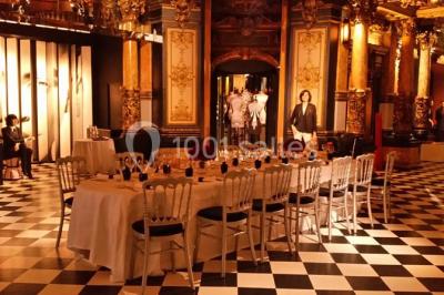 Salle élégante avec tables rondes dressées, chaises blanches et grand portrait en noir et blanc en arrière-plan.