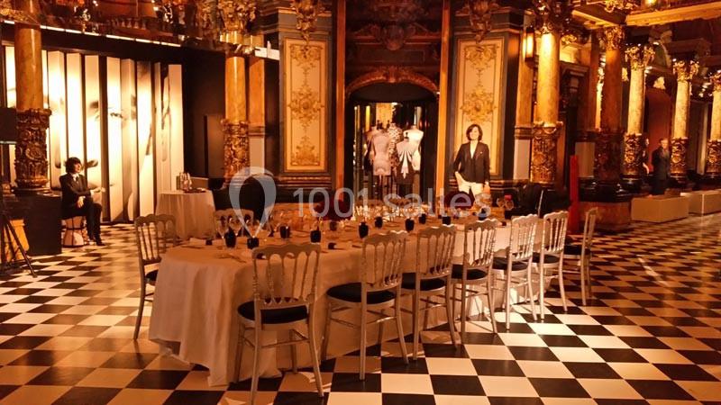 Salle décorée avec des colonnes dorées, un sol en damier noir et blanc, et une table dressée pour un dîner élégant.