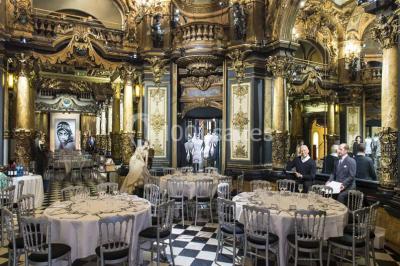 Salle élégante avec tables rondes dressées, chaises blanches et grand portrait en noir et blanc en arrière-plan.