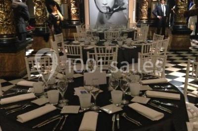 Salle élégante avec tables rondes dressées, chaises blanches et grand portrait en noir et blanc en arrière-plan.