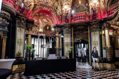 Salle élégante avec tables rondes dressées, chaises blanches et grand portrait en noir et blanc en arrière-plan.